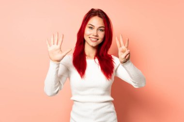 Pembe arka planda izole edilmiş genç kızıl saçlı kız dokuz parmaklı sayıyor.