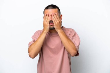 Beyaz arka planda izole edilmiş beyaz tenli genç adam gözlerini elleriyle kapatıyor.