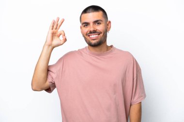 Beyaz arka planda izole edilmiş genç beyaz adam parmaklarıyla tamam işareti gösteriyor.