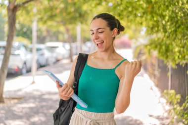 Dışarıda zaferi kutlayan genç ve güzel bir bayan öğrenci.
