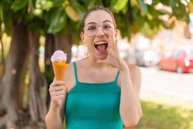 Açık havada kornet dondurması olan genç ve güzel bir kadın ağzı açık bağırıyor.