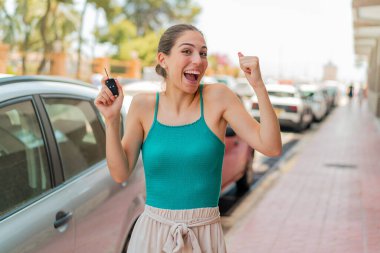 Açık havada elinde araba anahtarlarıyla genç ve güzel bir kadın zaferi kutluyor.
