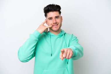 Beyaz arka planda izole edilmiş genç beyaz bir adam telefon jesti yapıyor ve ön tarafı işaret ediyor.