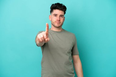 Mavi arka planda izole edilmiş genç beyaz adam parmağını kaldırıyor ve gösteriyor.
