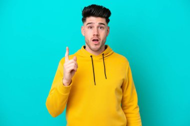 Kafkasyalı genç adam mavi arka planda izole edilmiş bir şekilde parmağını kaldırarak çözümü anlamaya çalışıyor.