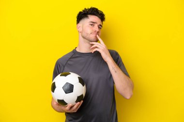 Yakışıklı genç futbolcu sarı arka planda izole edilmiş.