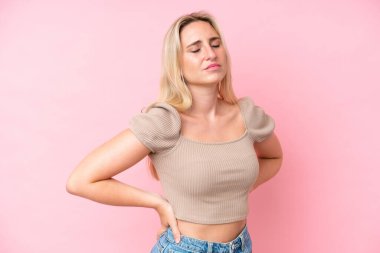 Pembe arka planda izole edilmiş beyaz bir kadın gayret gösterdiği için sırt ağrısı çekiyor.