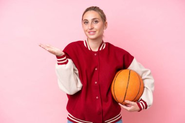 Genç basketbolcu beyaz kadın, pembe arka planda izole edilmiş, davet edildiği için ellerini yana uzatıyor.