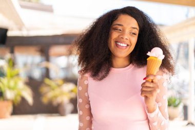 Genç Afrikalı Amerikalı kadın, açık havada kornet dondurması ve mutlu bir ifadeyle.