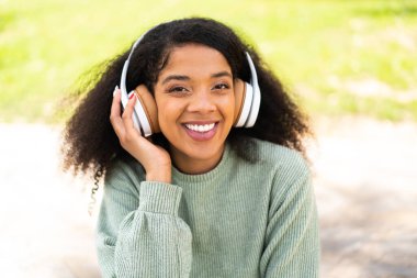 Genç Afrikalı Amerikalı kadın açık havada müzik dinliyor.