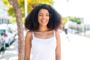 Genç Afrikalı Amerikalı kadın açık havada gözlüklü ve mutlu bir ifadeyle