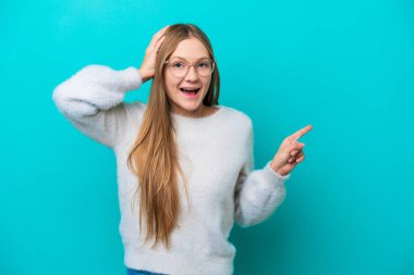 Mavi arka planda izole edilmiş genç bir Rus kadın. Şaşırmış ve işaret ediyor.