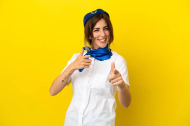Uçak hostesi kadın sarı arka planda izole edilmiş önü işaret ediyor ve gülümsüyor.