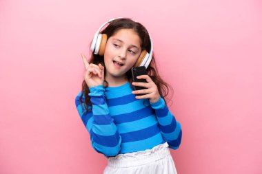 Pembe arka planda izole edilmiş küçük bir kız cep telefonuyla müzik dinliyor ve şarkı söylüyor