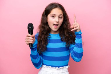 Pembe arka planda izole edilmiş bir mikrofonu eline alan küçük şarkıcı kız harika bir fikri işaret ediyor.