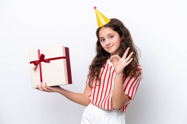 Beyaz arka planda izole edilmiş doğum günü hediyesi taşıyan genç beyaz kız gülümsüyor ve zafer işareti gösteriyor.