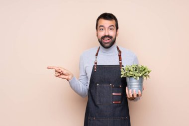 Arka planda bir bitkiyi tutan adam şaşırdı ve parmağını yana çevirdi.