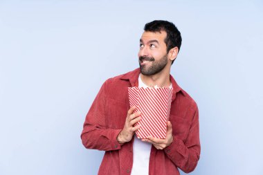 Mavi arka planda beyaz bir adam elinde koca bir kova patlamış mısır tutuyor.