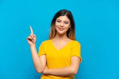 Mavi arka planda izole edilmiş genç bir Rus kızı en iyinin işareti olarak parmağını kaldırıyor ve gösteriyor.