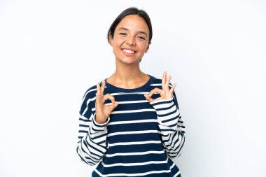 Beyaz arka planda izole edilmiş genç İspanyol kadın iki eliyle tamam işareti gösteriyor.