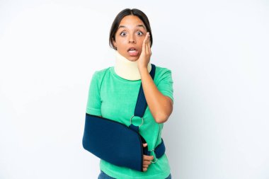 Boynunda boyunluk ve askısı olan genç İspanyol kadın beyaz arka planda, şaşırmış ve şok olmuş bir yüz ifadesi ile izole edilmiş.