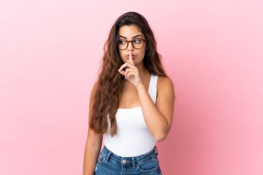 Pembe arka planda izole edilmiş beyaz bir kadın sessiz bir jest işareti gösteriyor. Parmağını ağzına sokuyor.
