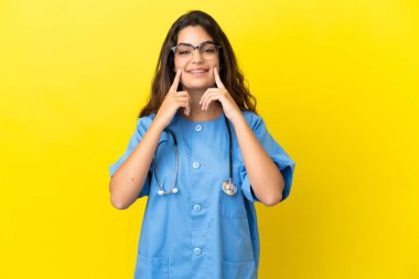 Sarı arka planda izole edilmiş genç cerrah kadın mutlu ve hoş bir ifadeyle gülümsüyor.