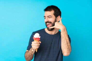 Kornet dondurması ile izole edilmiş mavi arka planı olan genç bir adam telefon jesti yapıyor. Bana geri dönüş işareti ver.