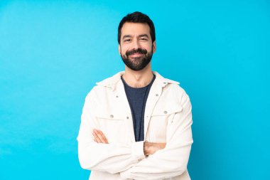 Mavi arka planda beyaz kadife ceketli genç ve yakışıklı bir adam kollarını ön cephede kavuşturuyor.