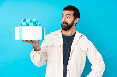 Büyük pastası olan genç ve yakışıklı bir adam izole edilmiş mavi arka planda