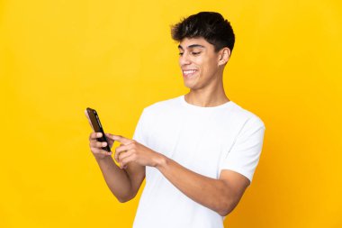 Sarı arka plan izole edilmiş genç adam cep telefonuyla bir mesaj ya da e-posta gönderiyor