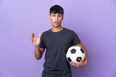 Genç futbolcu mor arka planda, şaşırmış ve şok olmuş bir yüz ifadesi var.