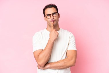 Pembe arka planda izole edilmiş genç beyaz adam yukarı bakarken şüphe duyuyor.