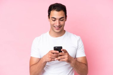 Pembe arka planda izole edilmiş genç beyaz adam cep telefonuyla mesaj ya da e-posta gönderiyor.