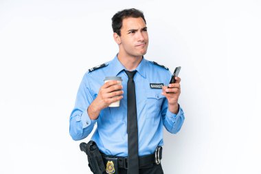 Young police caucasian man isolated on white background holding coffee to take away and a mobile while thinking something