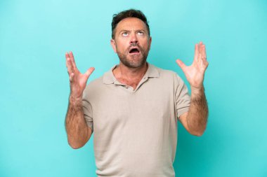 Mavi arka planda izole edilmiş orta yaşlı beyaz bir adam bunalıma girmiş.