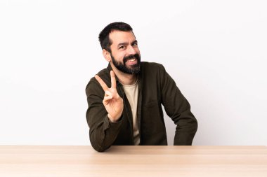 Masada sakallı, gülümseyen ve zafer işareti gösteren beyaz bir adam..