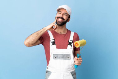 Yetişkin ressam mavi arka planda mutlu ve hoş bir ifadeyle gülümsüyor.