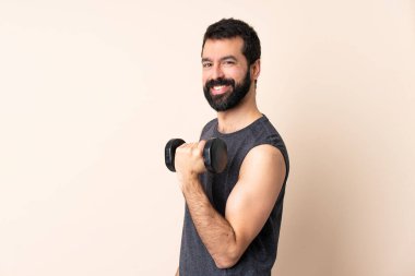 Sakallı, beyaz tenli, halter kaldıran, izole edilmiş arka planda kolları bağlı ve ileriye bakan bir sporcu.