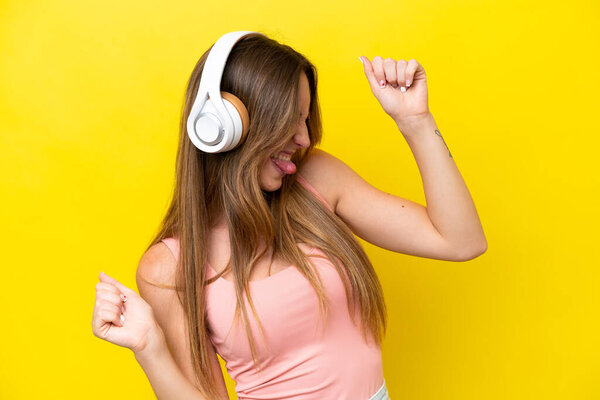 Young caucasian woman isolated on yellow background listening music and dancing