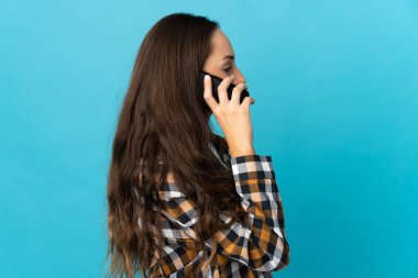 İzole edilmiş mavi arka planda genç bir İspanyol kadın cep telefonuyla sohbet ediyor.
