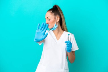 Beyaz dişçi kadının elinde mavi arka planda izole edilmiş aletler var dur hareketi yapıyor ve hayal kırıklığına uğruyor.