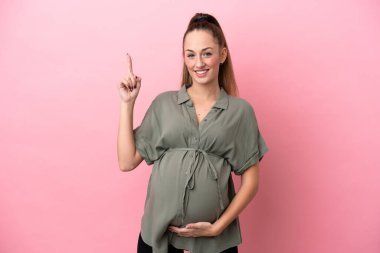 Pembe arka planda izole edilmiş genç bir kadın hamile ve yukarıya bakıyor.