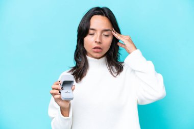 Mavi arka planda baş ağrısıyla izole edilmiş bir nişan yüzüğü tutan genç İspanyol kadın.