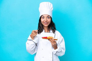 Mavi arka planda saşimi tutan genç İspanyol aşçı kadın şaşırmış ve ön tarafı işaret ediyor.