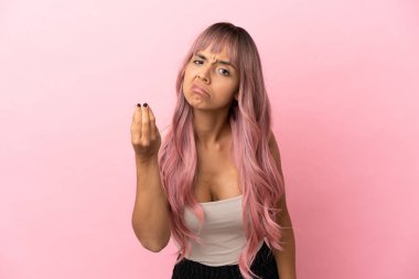 Pembe saçlı melez bir kadın pembe arka planda İtalyan jesti yapıyor.
