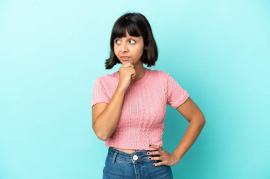 Genç melez kadın mavi arka planda izole edilmiş bir şekilde bakarken bir fikir düşünüyor.