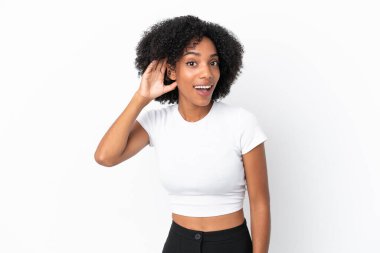 Genç Afrikalı Amerikalı bir kadın beyaz arka planda izole edilmiş bir şekilde elini kulağına koyarak bir şeyler dinliyor.