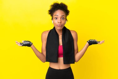 Sarı arka planda izole edilmiş genç Afrikalı kadın ellerini kaldırırken kuşkuları var.