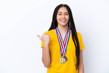 Saçları örgülü ve madalyalı genç bir kız pembe arka planda bir ürün sunmak için kenarı işaret ediyor.